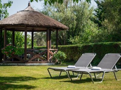 Zwei Liegestühle auf einer Wiese vor einem Pavillon in einem grünen Garten.