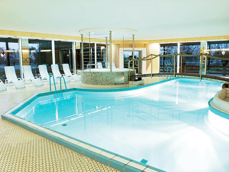 Jasny basen wewnętrzny z leżakami i jacuzzi z boku w hotelu.