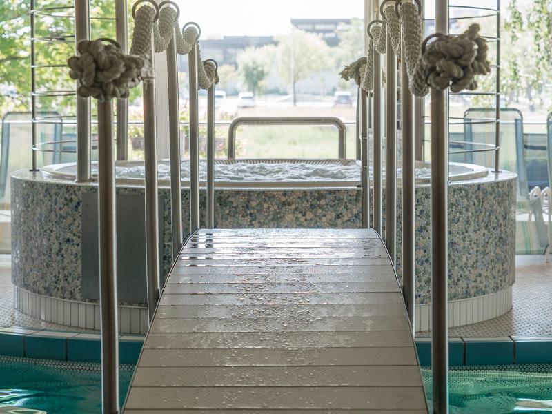 Pomost z poręczami prowadzący do jacuzzi w jasnej strefie wellness.