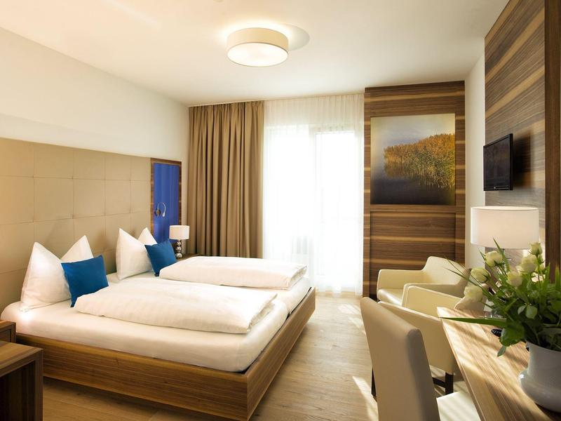 Jasny pokój hotelowy z dwoma łóżkami pojedynczymi, częścią wypoczynkową i dużym oknem z zasłonami.