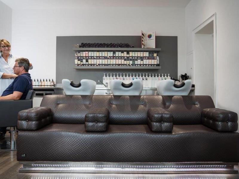 Nowoczesne wnętrze salonu fryzjerskiego z umywalkami i skórzaną sofą na pierwszym planie.