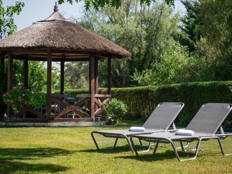 Dwa leżaki przed drewnianym pawilonem z dachem ze strzechy w ogrodzie.