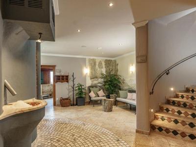 Hall d'hôtel lumineux avec escalier en pierre, canapé, plantes et télévision en arrière-plan.