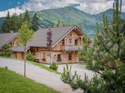 Maison en bois dans les montagnes avec herbe verte et arbres au premier plan.