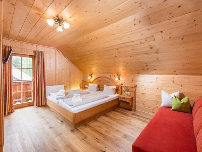 Chambre confortable avec murs en bois, lit double, canapé rouge et balcon avec vue.