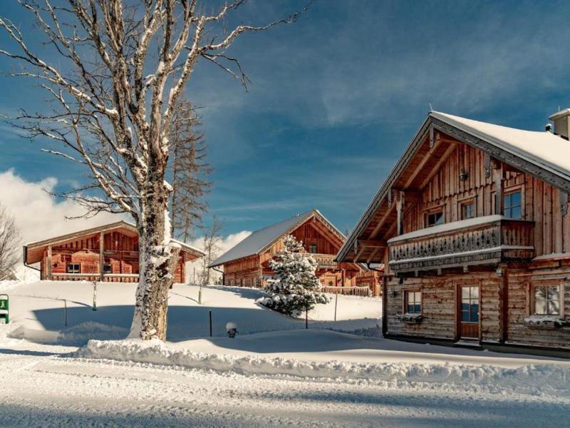 Chalets en bois enneigés sous un ciel bleu dans une station d'hiver.