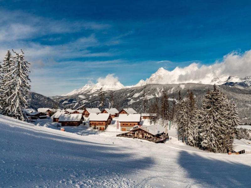 Paysage montagneux enneigé avec des maisons en bois et des sapins sous un ciel bleu.