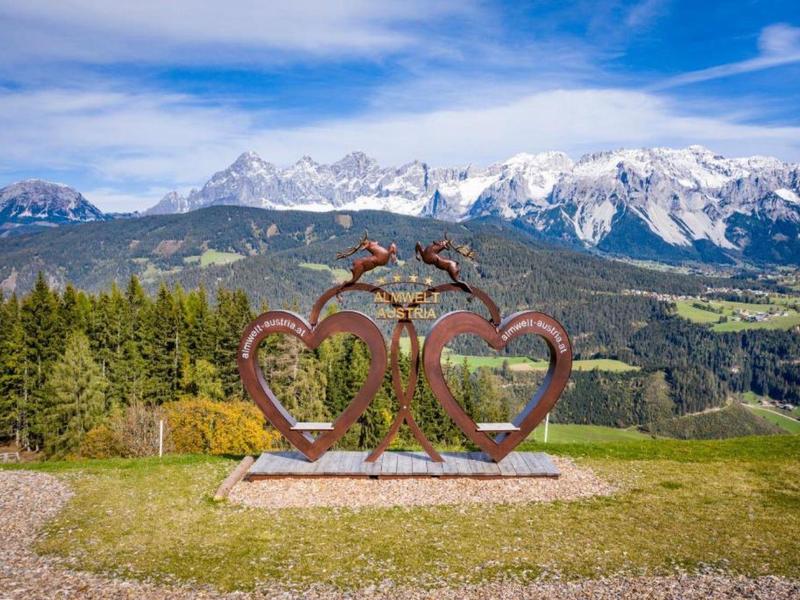 Sculpture avec deux cœurs et un oiseau devant des montagnes enneigées dans un paysage verdoyant