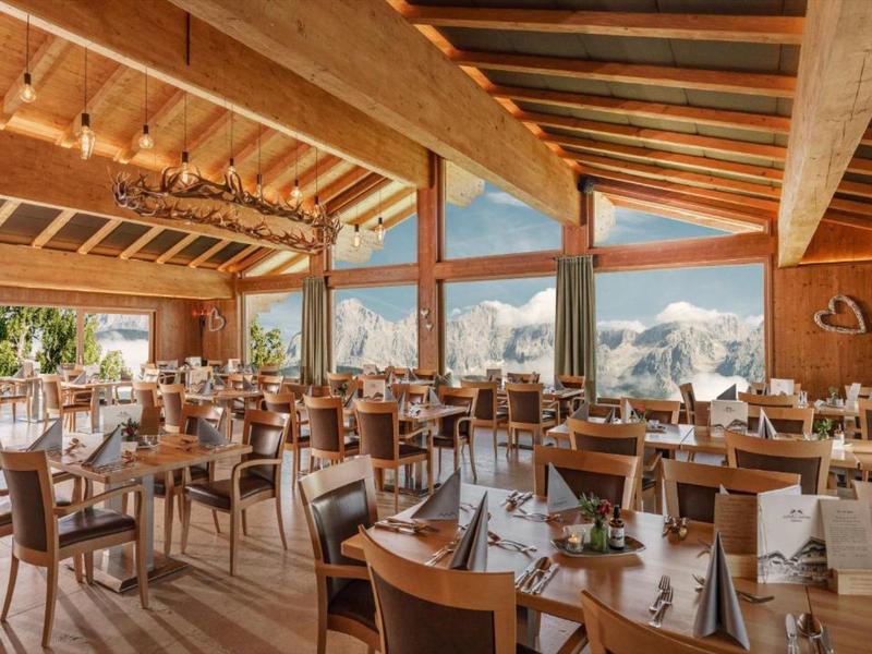 Restaurant de montagne lumineux avec plafond en bois, grandes fenêtres et vue sur des sommets enneigés.