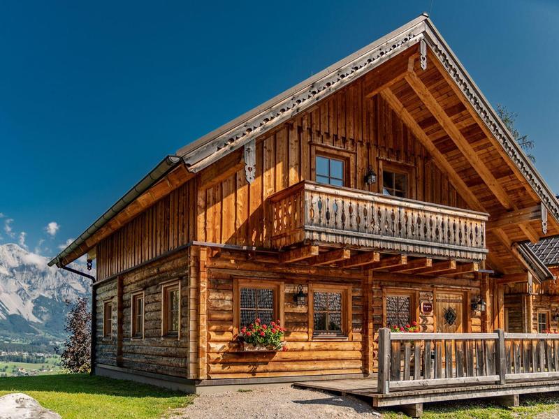 Chalet en bois chaleureux avec balcon dans un paysage montagneux pittoresque sous un ciel clair.