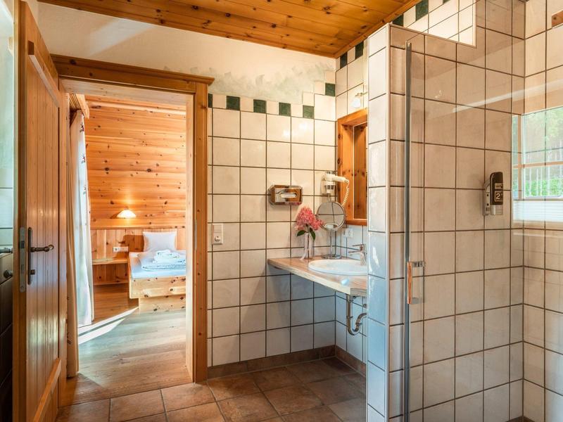 Salle de bain carrelée claire avec plafond en bois et vue sur une pièce avec sauna.