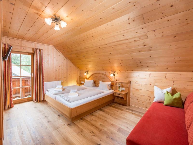 Chambre confortable avec murs en bois, lit double, canapé rouge et balcon avec vue.