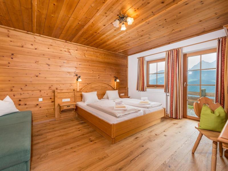 Chambre d'hôtel lumineuse avec murs en bois, lit double, canapé et fenêtre avec vue sur les montagnes.