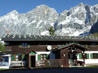 Alpenhotel mit Holzfassade vor schneebedeckten Bergen unter klarem Himmel.