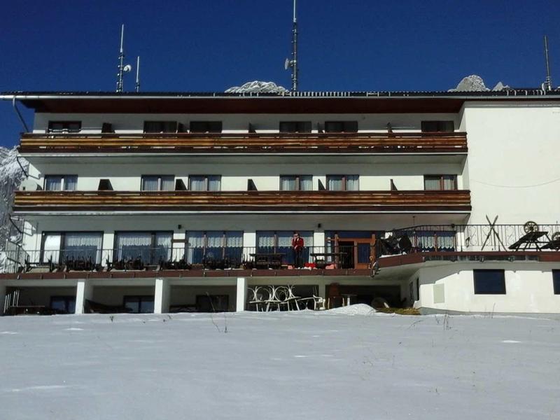 Nowoczesny budynek hotelowy z balkonem na tle ośnieżonych gór i czystego nieba.