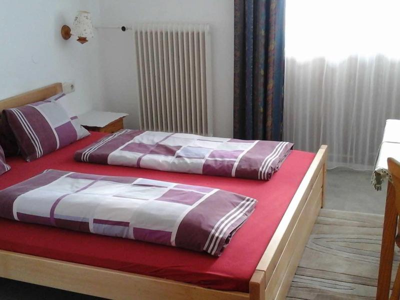 Prosta sypialnia z podwójnym łóżkiem, bordową pościelą i drewnianą podłogą.