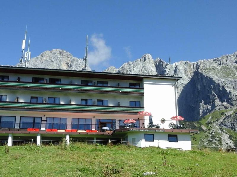 Górski hotel z wieloma piętrami przed stromymi skalnymi ścianami i niebieskim niebem.