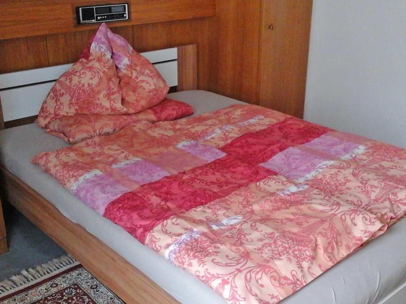 Łóżko pojedyncze z różową, wzorzystą pościelą w drewnianej ramie na dywanie.