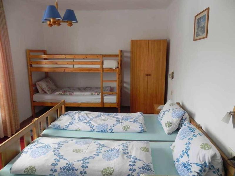 Prosto urządzone pokoje hotelowe z łóżkiem piętrowym, podwójnym łóżkiem i małą szafą.