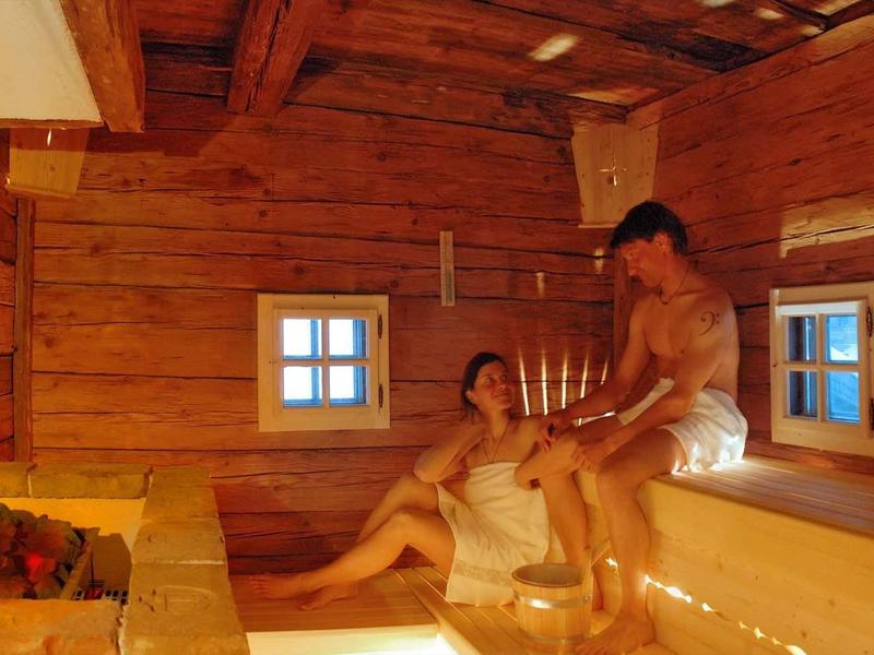 Twee mensen ontspannen in een houten sauna met kleine ramen en zacht licht.