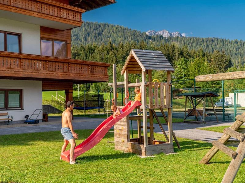 Speeltuin met glijbaan voor hotelgebouw in een bergachtig landschap.