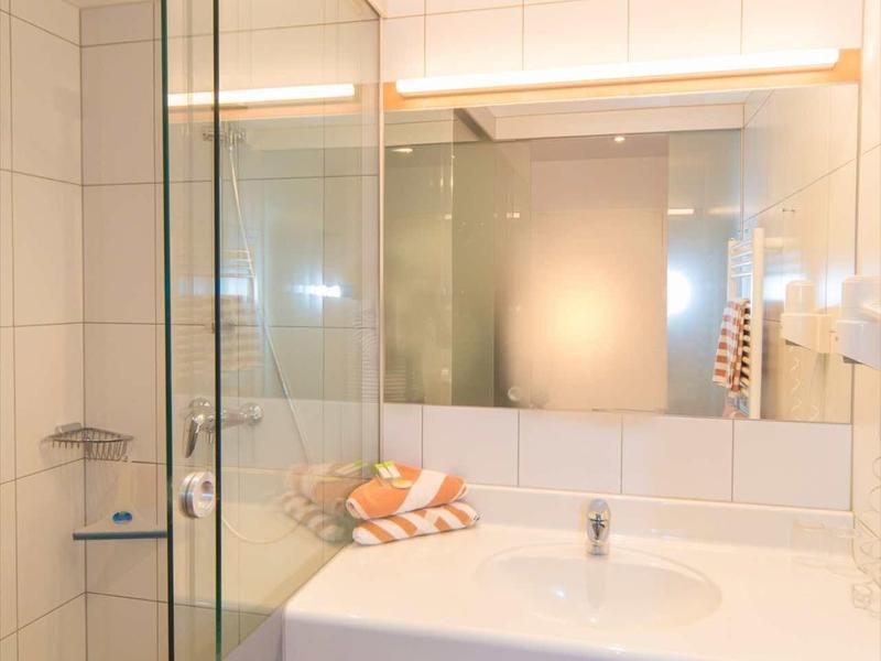 Lichte hotelbadkamer met grote spiegelwand, wastafel en aparte glazen douche.