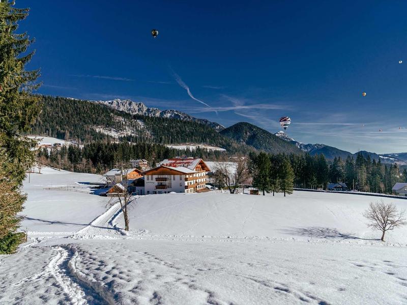 Winterlandschap met besneeuwd veld, bomen, huizen en paragilders aan de lucht.