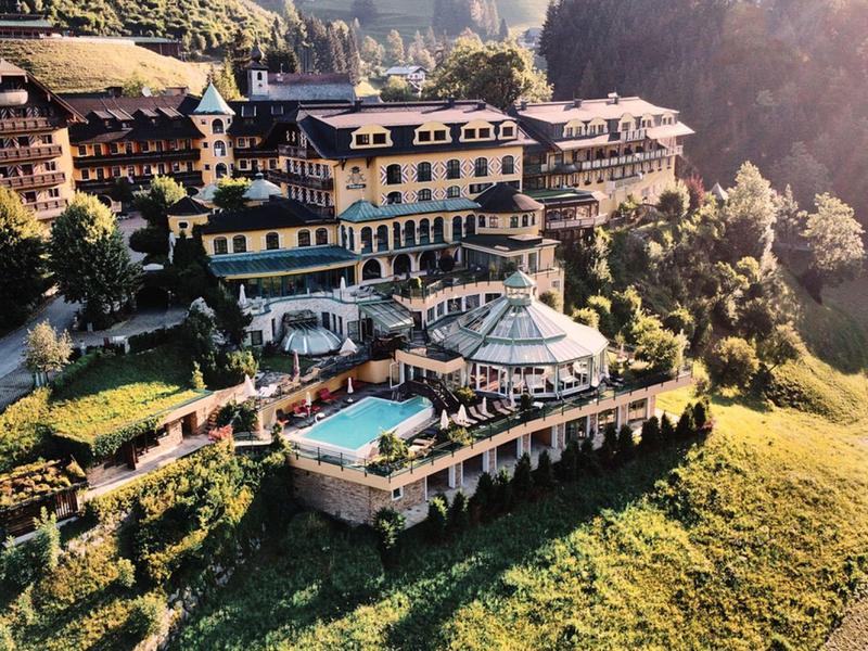 Velký hotelový resort na kopci s bazénem, obklopen lesy a loukami na slunci