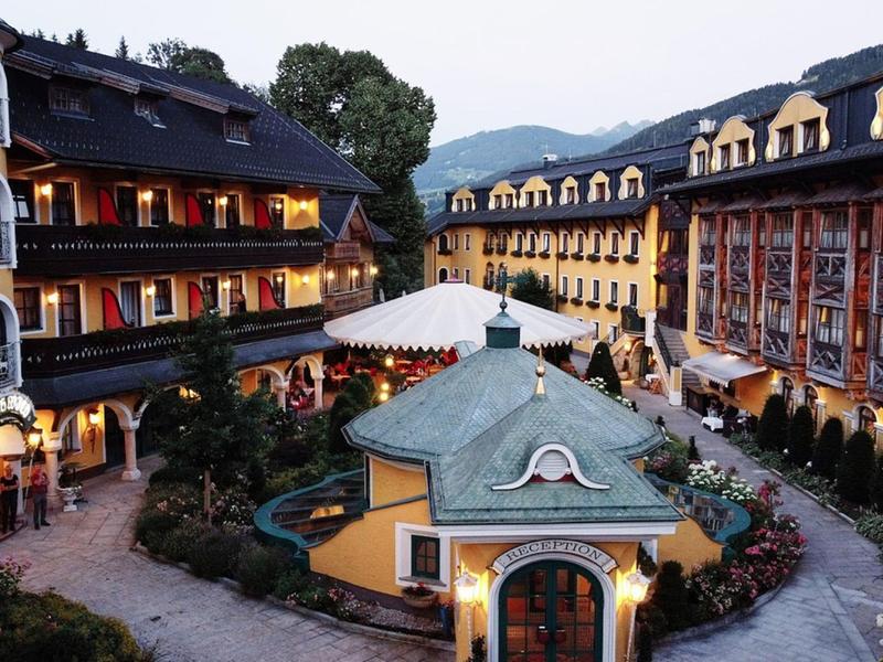 Hotelový komplex se žlutými budovami, dvorem se zahradou a pavilonem v horách.