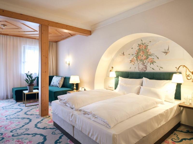 Světý hotelový pokoj s velkou postelí, měkkými koberci a útulným posezením za denního světla.