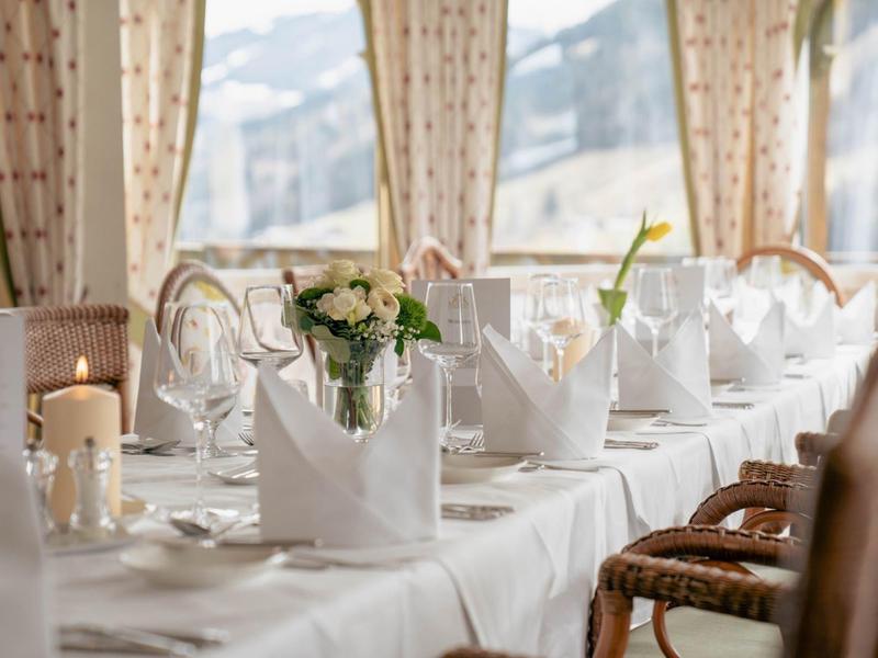 Elegantně prostřený stůl s bílými ubrousky a květinami v světlé místnosti s výhledem na hory.