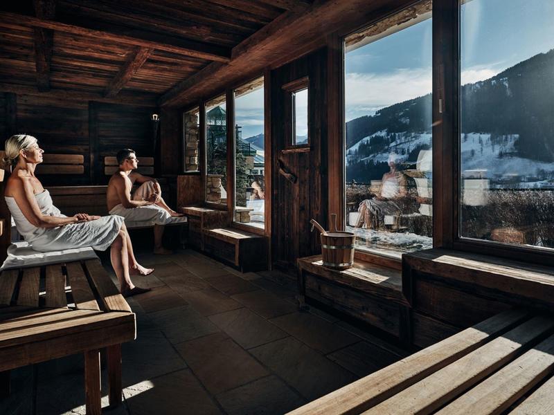 Tři lidé relaxují v dřevěné odpočívárně s výhledem na hory a slunečním světlem