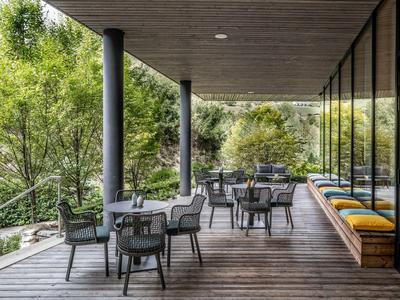 Überdachte Hotelterrasse mit Sitzgruppen und Blick auf grüne Bäume.