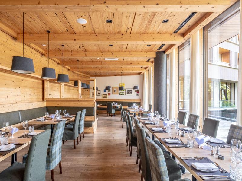 Modern restaurant met houten balkenplafond, grote ramen en gedekte tafels voor gasten.