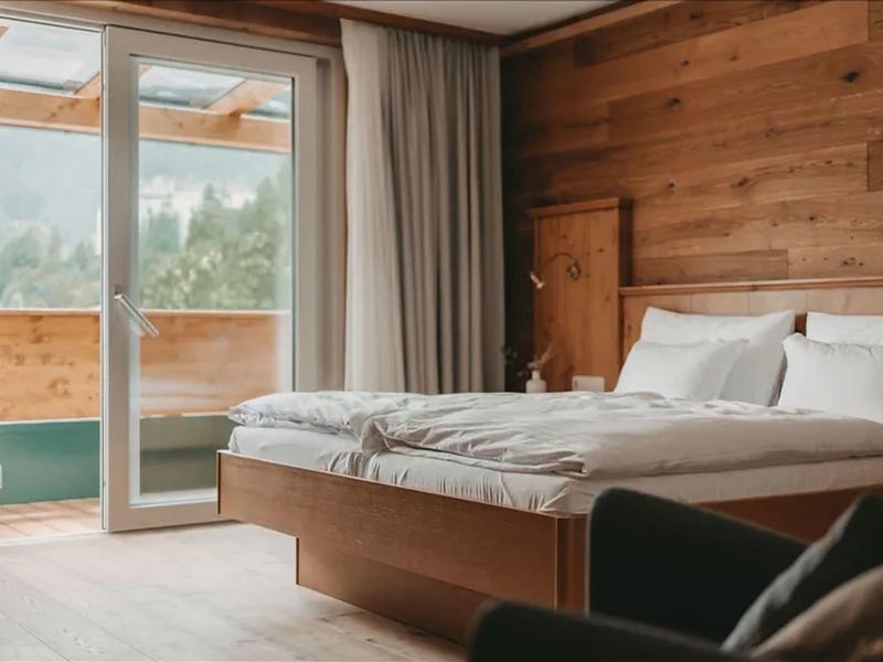 Bright bedroom with wooden walls, double bed, and balcony door overlooking greenery.