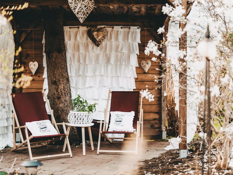 Cozy terrace with two wooden chairs and table in front of rustic wooden wall.