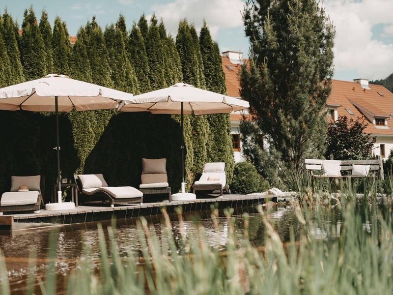 Relaxation area with lounge chairs and umbrellas in front of a house and trees.