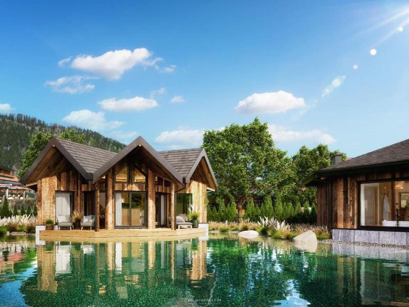 Modern wooden houses beside a clear lake in a green landscape under a blue sky.