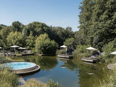 Piscina natural con bañeras redondas de hidromasaje y sombrillas en entorno forestal verde.