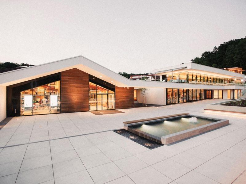 Hotel moderno con grandes fachadas de vidrio y techo plano, rodeado por una terraza con piscina.