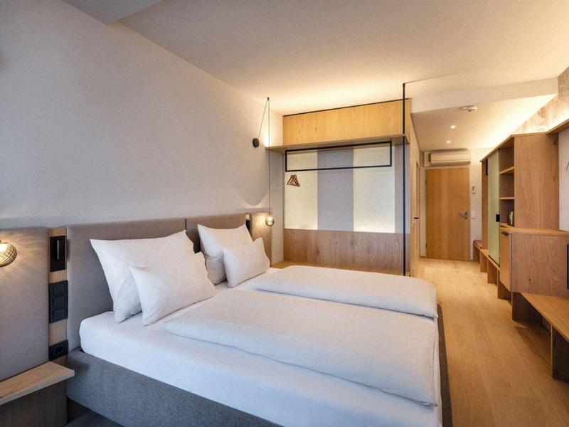 Habitación de hotel moderna con dos camas, muebles de madera y luz cálida.