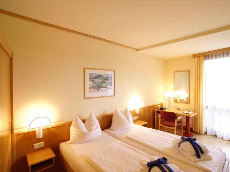 Habitación de hotel luminosa con dos camas individuales, lámparas de noche y escritorio con espejo.