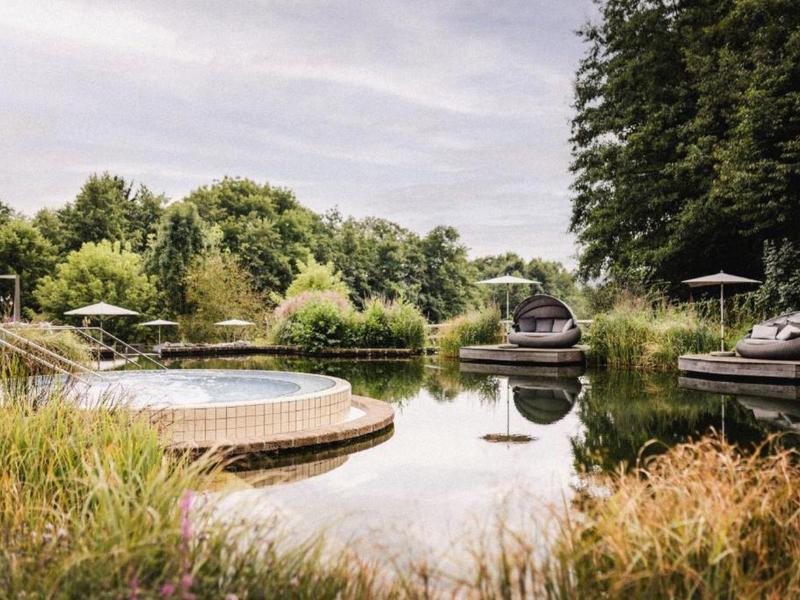 Piscina natural con terraza de madera y zonas de descanso acogedoras en un jardín verde.