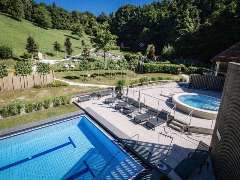 Área de ocio con piscina, jacuzzi y tumbonas en un paisaje verde y montañoso.