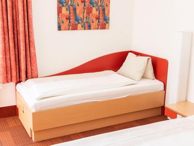 Ein einfaches Hotelzimmer mit Einzelbett, roten Akzenten und einem bunten Bild an der Wand.