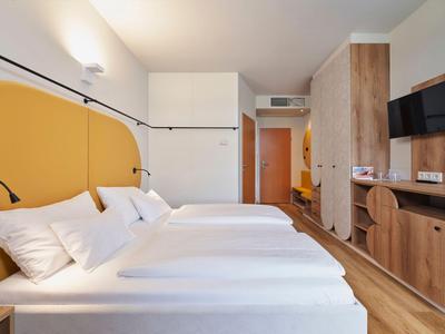 Modernes Hotelzimmer mit zwei Einzelbetten, Holzmöbeln und Wandfernseher.
