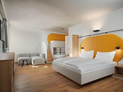 Modernes Hotelzimmer mit großem Bett und auffälliger orangefarbener Wandgestaltung.