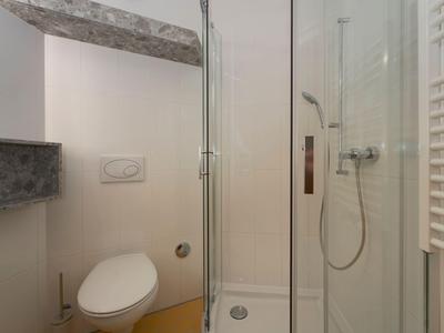 Kompakte Badezimmer mit Duschkabine, weißer Toilette und Handtuchheizkörper unter Holzbalken.
