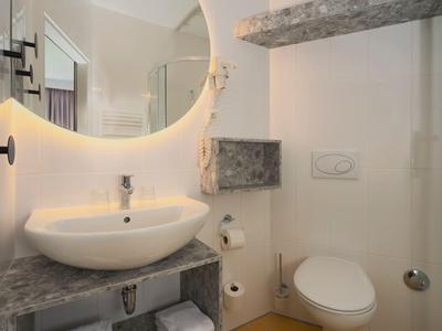 Modernes Hotelbadezimmer mit rundem Spiegel, Waschbecken und Toilette in neutralen Tönen.