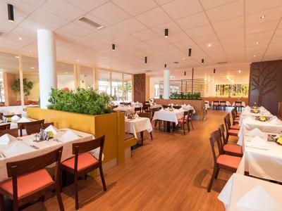 Heller Hotelrestaurantbereich mit Holzboden, weißen Tischdecken und modernen Holzstühlen.